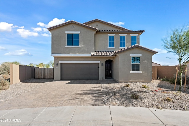 mediterranean / spanish home featuring a tile roof, an attached garage, fence, decorative driveway, and stucco siding