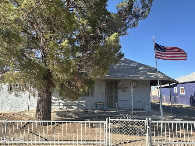 view of front facade with roof with shingles, a gate, fence, and stucco siding