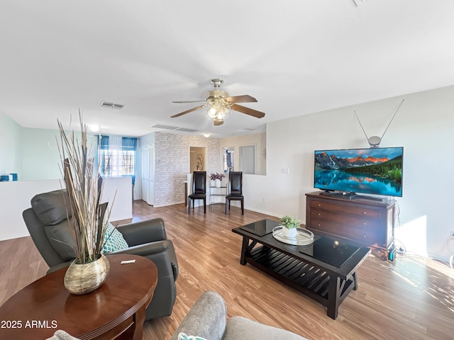 living room with light hardwood / wood-style flooring, ceiling fan, and brick wall