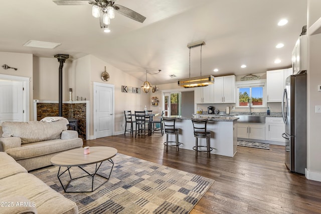 living room featuring lofted ceiling, sink, a wood stove, dark hardwood / wood-style flooring, and ceiling fan