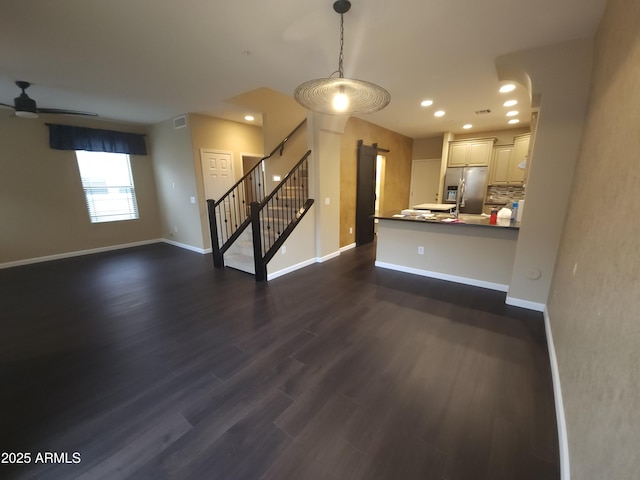 unfurnished living room with ceiling fan, dark wood-type flooring, and a barn door