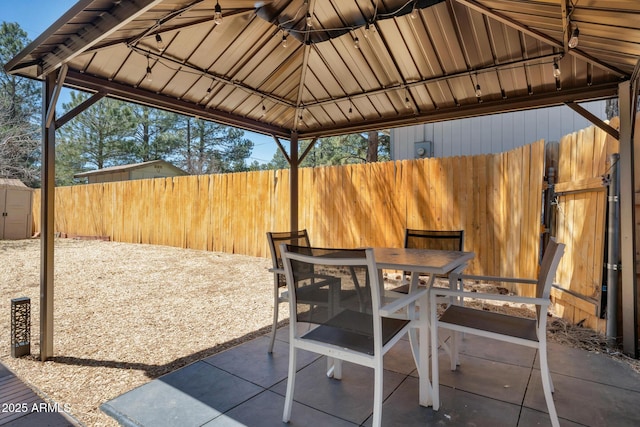 view of patio with a gazebo, a fenced backyard, an outdoor structure, outdoor dining area, and a storage unit