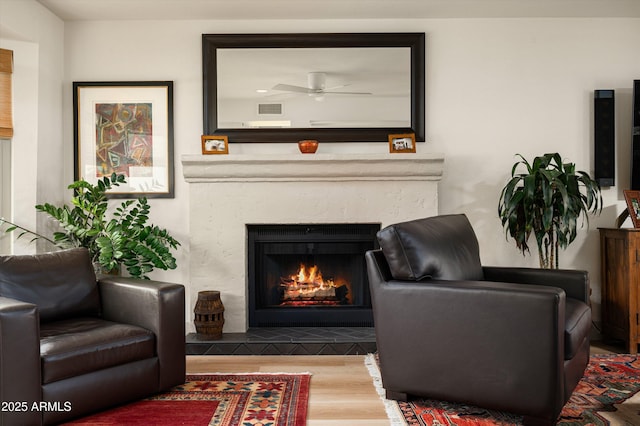 8068 E Del Trigo Rd, Scottsdale, AZ 85258 - sitting room featuring a ceiling fan, a warm lit fireplace, and wood finished floors