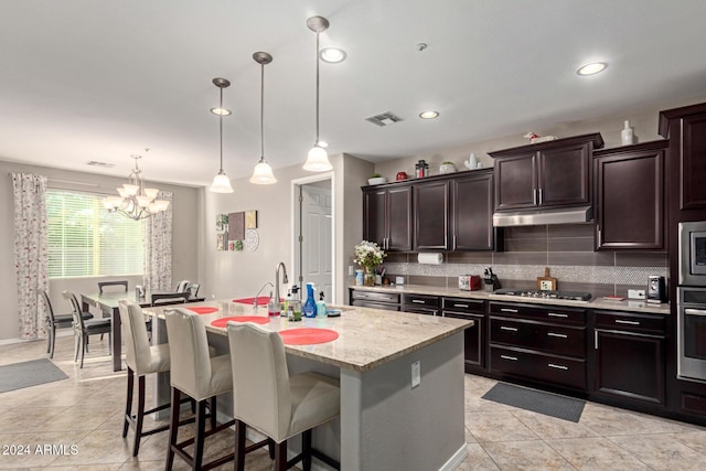 kitchen featuring decorative backsplash, pendant lighting, stainless steel appliances, and a kitchen island with sink