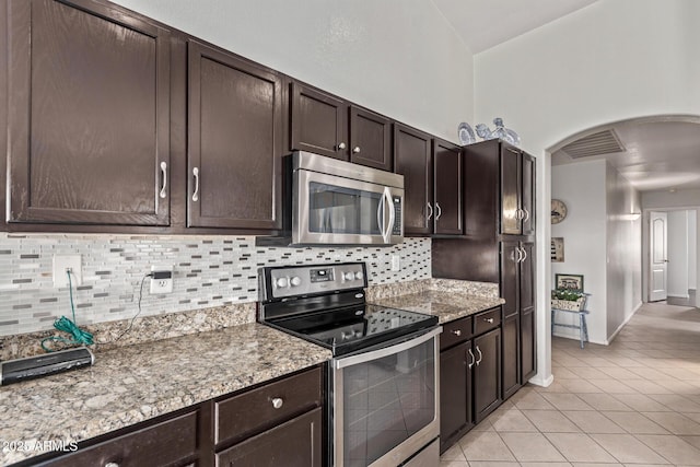 kitchen featuring light stone countertops, appliances with stainless steel finishes, backsplash, and dark brown cabinetry