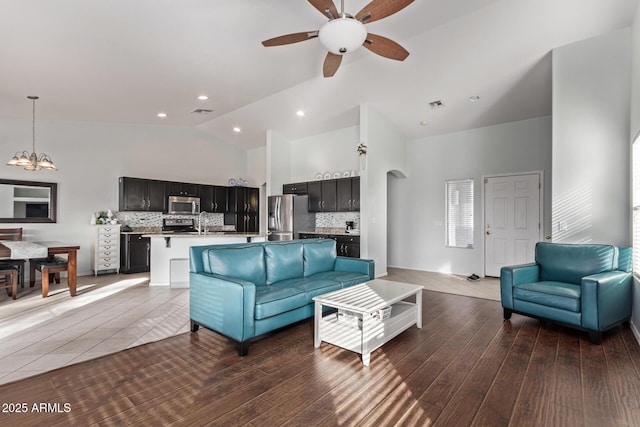 living room with sink, dark wood-type flooring, ceiling fan with notable chandelier, and high vaulted ceiling