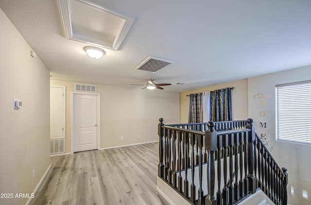 hallway with an upstairs landing, attic access, light wood-style flooring, baseboards, and visible vents