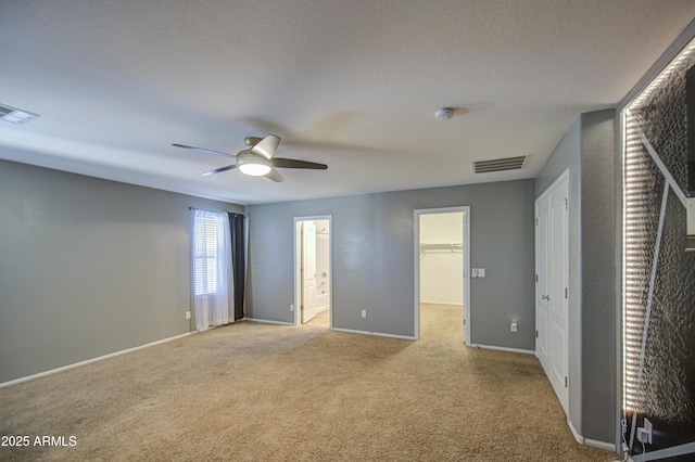 unfurnished bedroom with a walk in closet, carpet flooring, and visible vents
