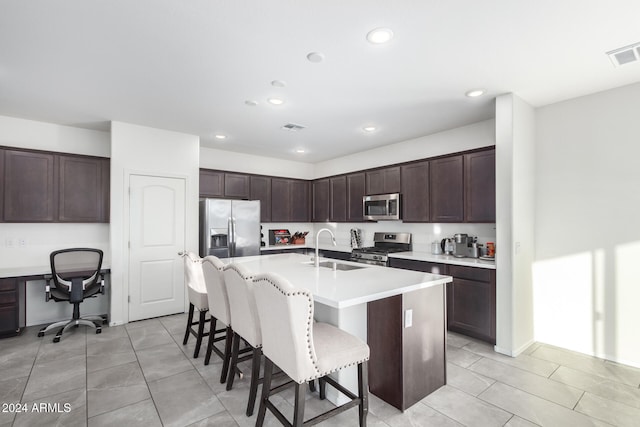 kitchen with sink, a breakfast bar area, a center island with sink, light tile patterned floors, and appliances with stainless steel finishes