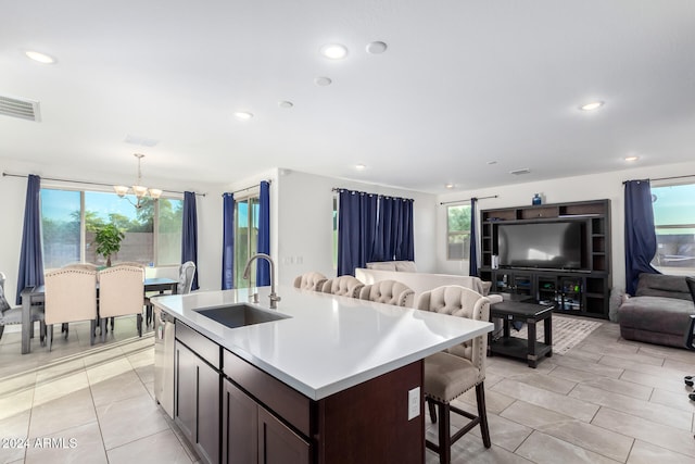 kitchen with sink, a notable chandelier, decorative light fixtures, dark brown cabinets, and a center island with sink