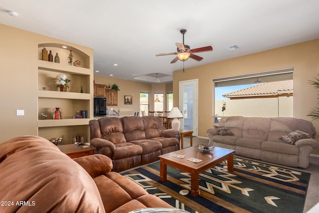 living room with built in shelves and ceiling fan