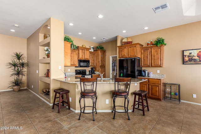 kitchen with kitchen peninsula, black appliances, a breakfast bar, light stone counters, and built in shelves