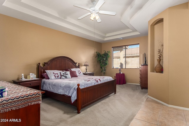 bedroom with light carpet, a tray ceiling, and ceiling fan