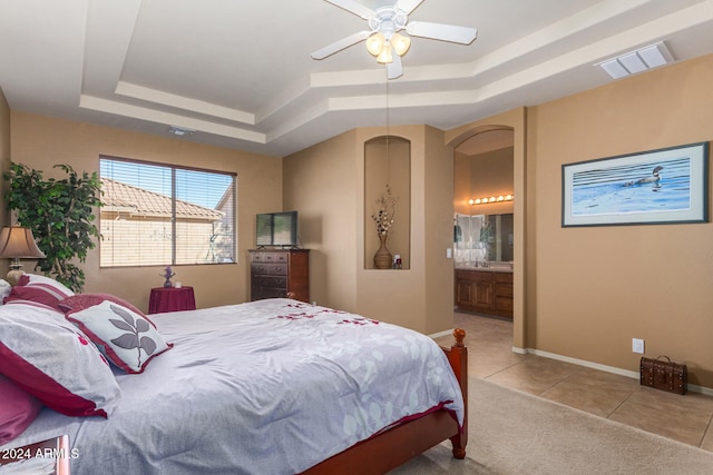 tiled bedroom featuring ensuite bath, a tray ceiling, and ceiling fan