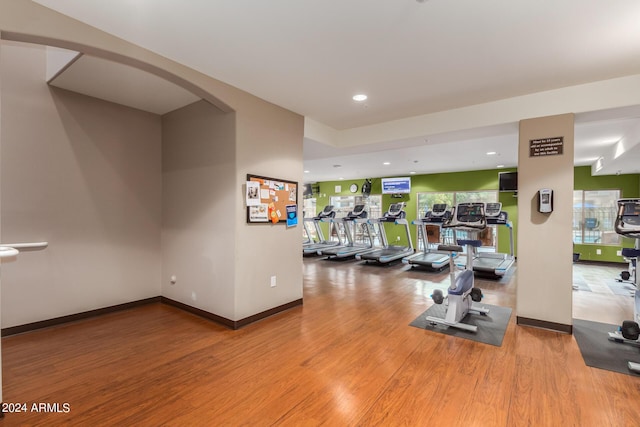 gym with arched walkways, recessed lighting, baseboards, and wood finished floors