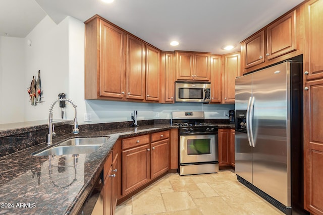 kitchen with a sink, appliances with stainless steel finishes, brown cabinets, dark stone countertops, and stone tile flooring