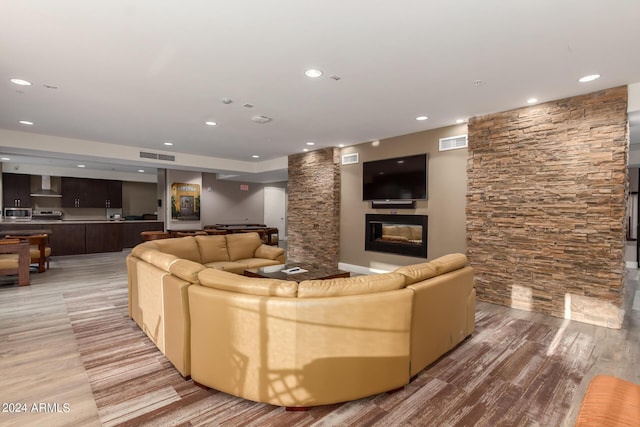 living area with a glass covered fireplace, visible vents, light wood finished floors, and recessed lighting