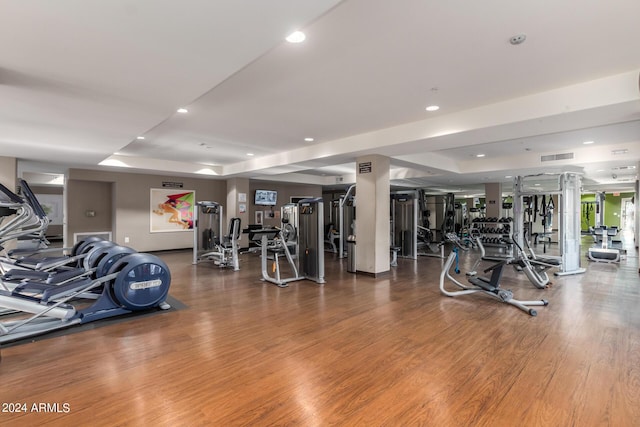 gym featuring visible vents, a raised ceiling, wood finished floors, and recessed lighting