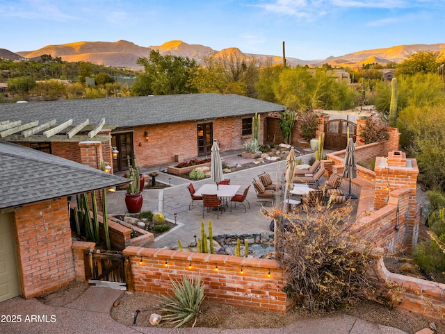 rear view of property featuring brick siding, a shingled roof, a gate, a patio area, and a mountain view