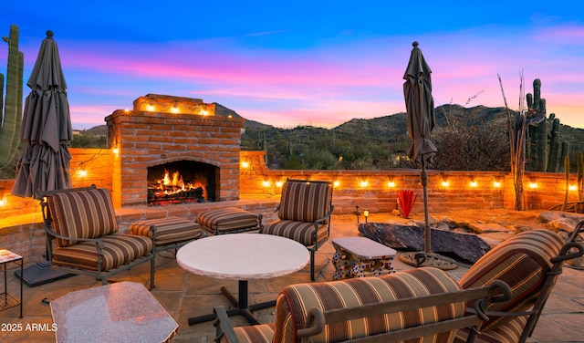 patio terrace at dusk featuring an outdoor brick fireplace and a mountain view