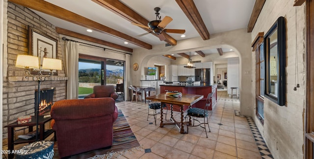 dining room featuring arched walkways, a ceiling fan, a brick fireplace, a mountain view, and beamed ceiling