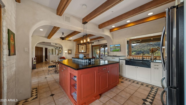 kitchen featuring arched walkways, a sink, beam ceiling, freestanding refrigerator, and dark countertops