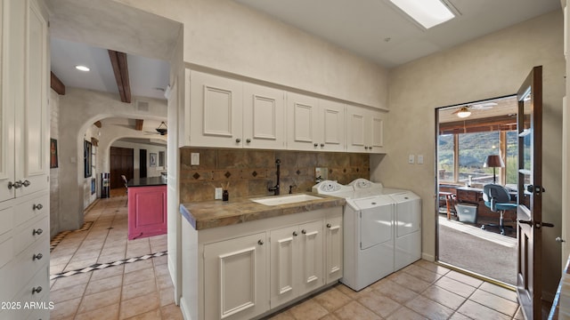 washroom featuring cabinet space, arched walkways, a ceiling fan, washing machine and dryer, and a sink