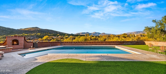 outdoor pool with a patio area, an outdoor brick fireplace, a mountain view, and a lawn