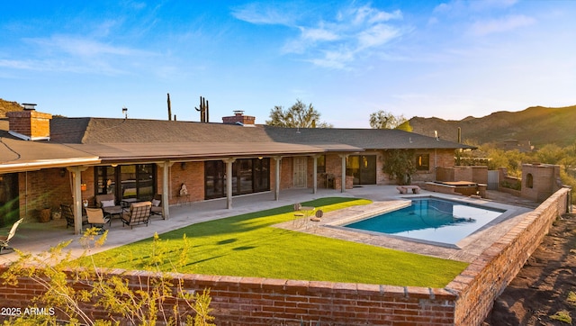 back of house with a mountain view, a patio, a chimney, and a lawn