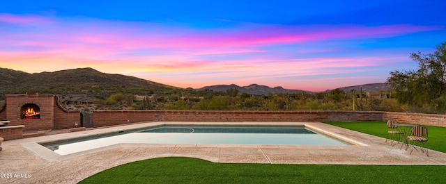 pool at dusk featuring a patio area, an outdoor brick fireplace, a mountain view, and an outdoor pool