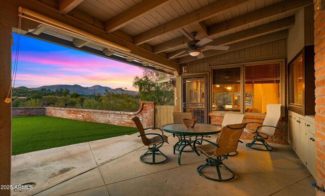 patio terrace at dusk featuring ceiling fan, a mountain view, and a lawn