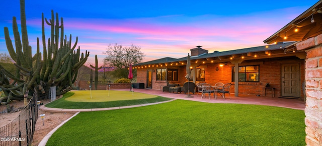 exterior space with brick siding, fence, a yard, a chimney, and a patio area