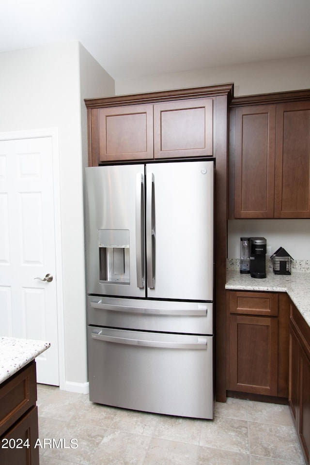 kitchen with dark brown cabinets, light stone counters, and stainless steel refrigerator with ice dispenser