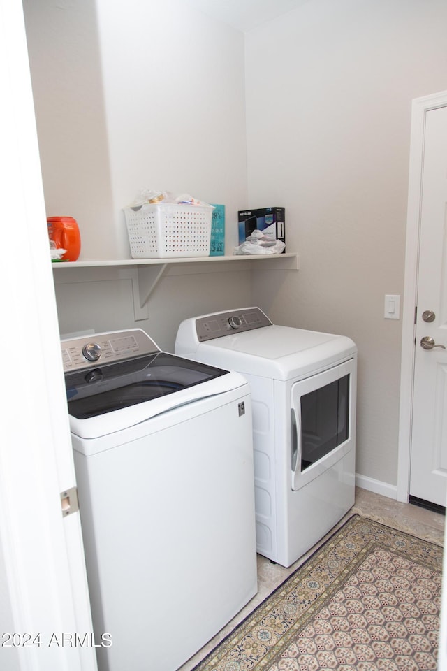 clothes washing area with laundry area, baseboards, washer and clothes dryer, and light tile patterned flooring