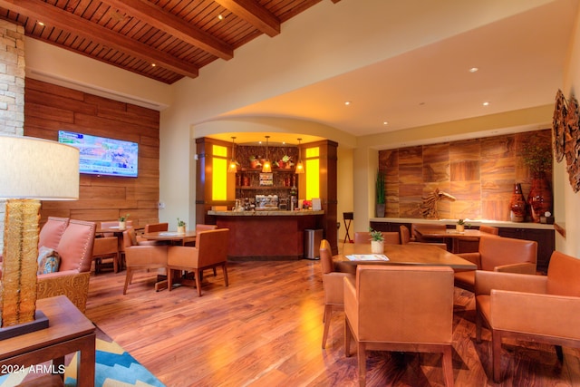 living room featuring wood walls, wood finished floors, a community bar, wood ceiling, and beamed ceiling