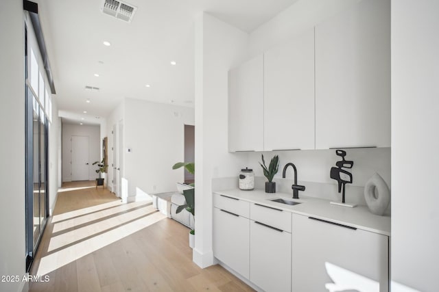 bar with white cabinets, light hardwood / wood-style floors, and sink