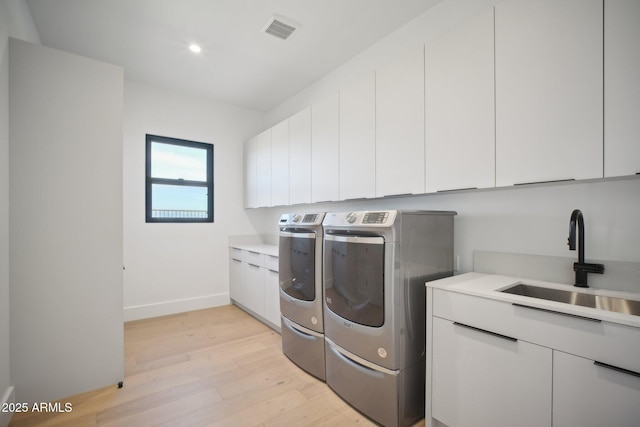 laundry room with separate washer and dryer, sink, cabinets, and light wood-type flooring