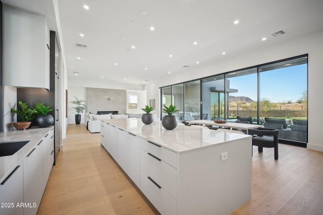 kitchen featuring a large island, light stone countertops, white cabinetry, and light hardwood / wood-style flooring