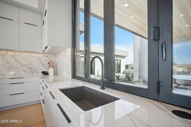 kitchen with backsplash, white cabinets, sink, light hardwood / wood-style flooring, and light stone counters