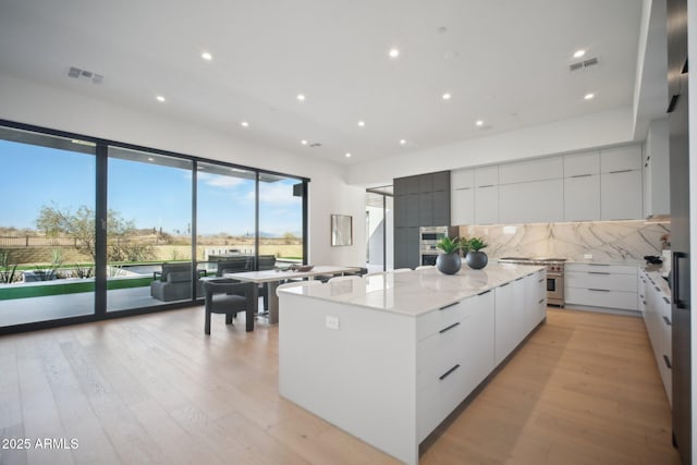 kitchen with light stone countertops, backsplash, a spacious island, light hardwood / wood-style flooring, and white cabinetry