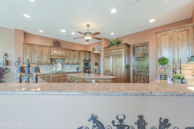 kitchen with light stone counters, built in appliances, kitchen peninsula, and decorative backsplash