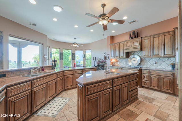 kitchen featuring light stone countertops, a kitchen island, sink, and decorative backsplash