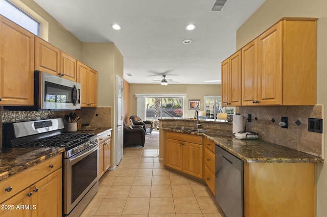 kitchen with sink, light tile patterned floors, appliances with stainless steel finishes, kitchen peninsula, and dark stone counters