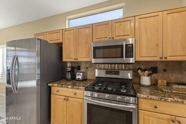 kitchen with backsplash, stainless steel appliances, light brown cabinets, and dark stone countertops