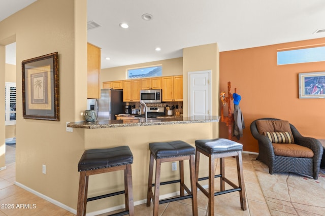 kitchen featuring a breakfast bar, light tile patterned floors, dark stone counters, kitchen peninsula, and stainless steel appliances