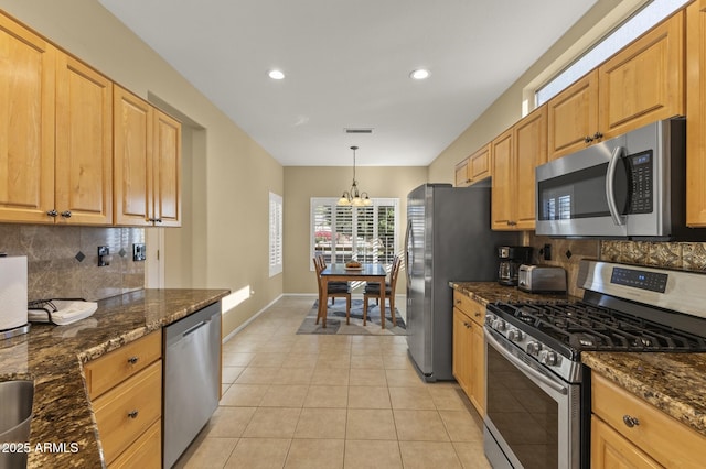 kitchen featuring stainless steel appliances, light tile patterned floors, hanging light fixtures, and dark stone countertops