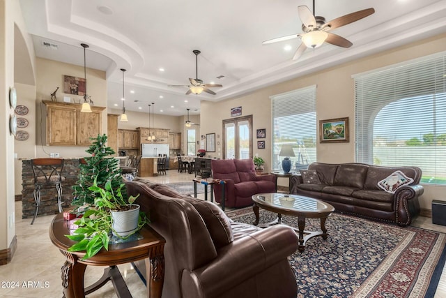 living room featuring light tile patterned floors, a raised ceiling, ceiling fan, and a healthy amount of sunlight