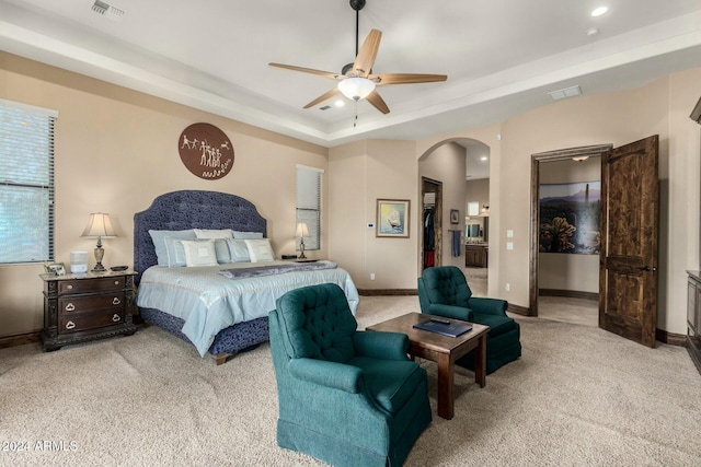 bedroom with ceiling fan, a closet, light carpet, and a tray ceiling