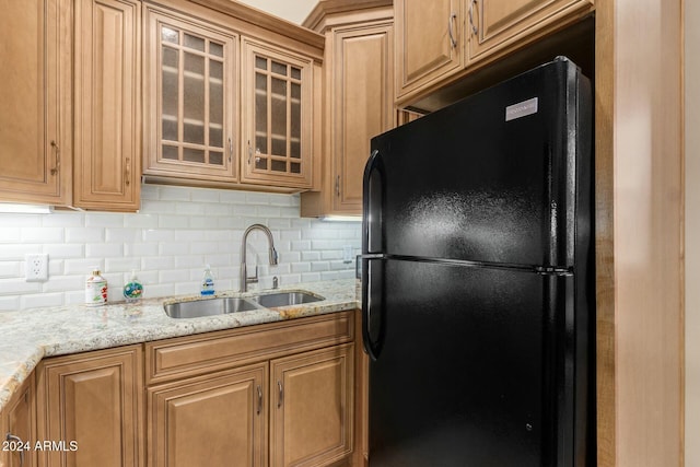 kitchen with backsplash, light stone counters, black fridge, and sink