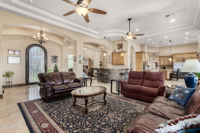 living room featuring ceiling fan with notable chandelier and a tray ceiling